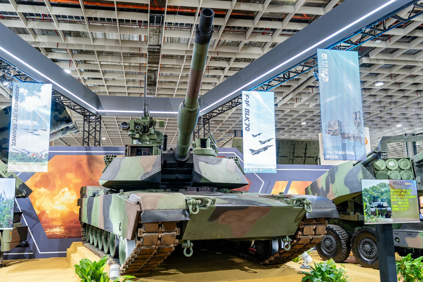 Camouflage military tank sits on a platform at an exhibition.