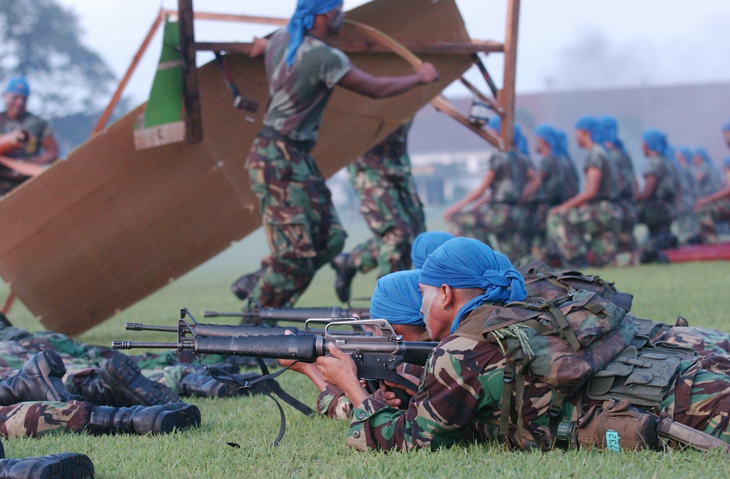 Soldiers in camouflage gear training on a grassy field.